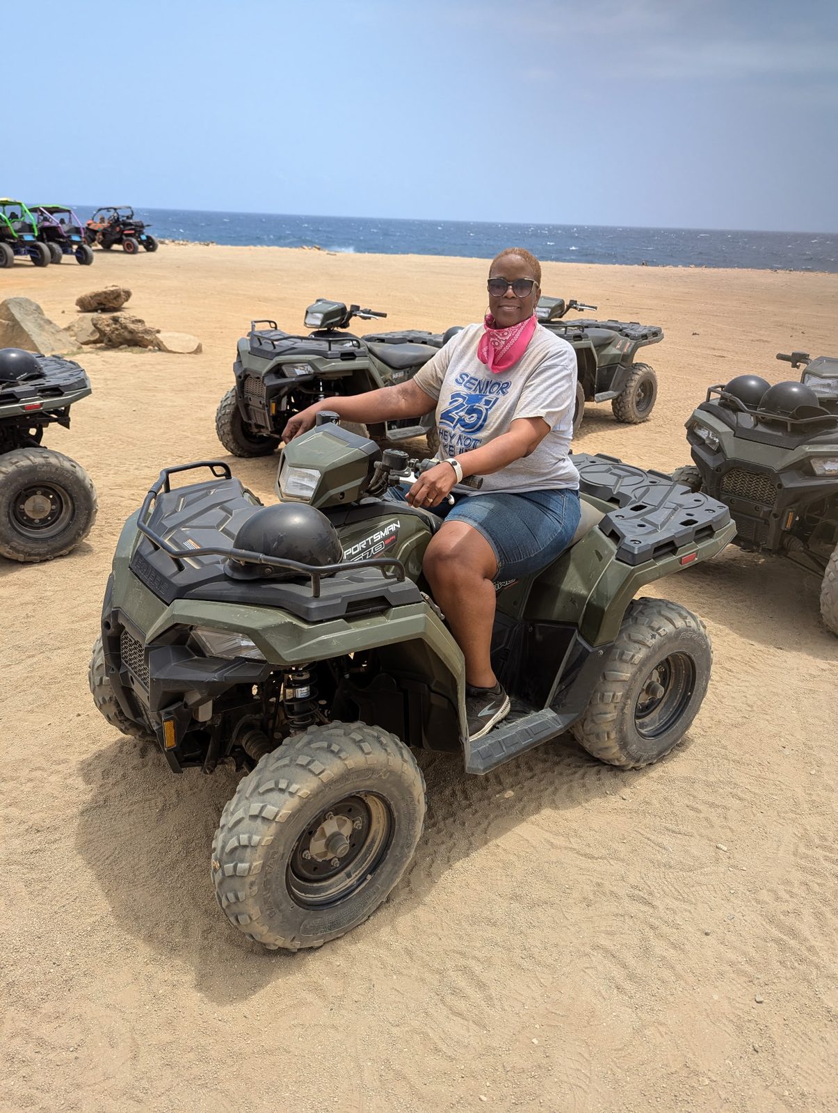 Carol seated on an ATV on a sandy beach with more ATVs lined up behind her