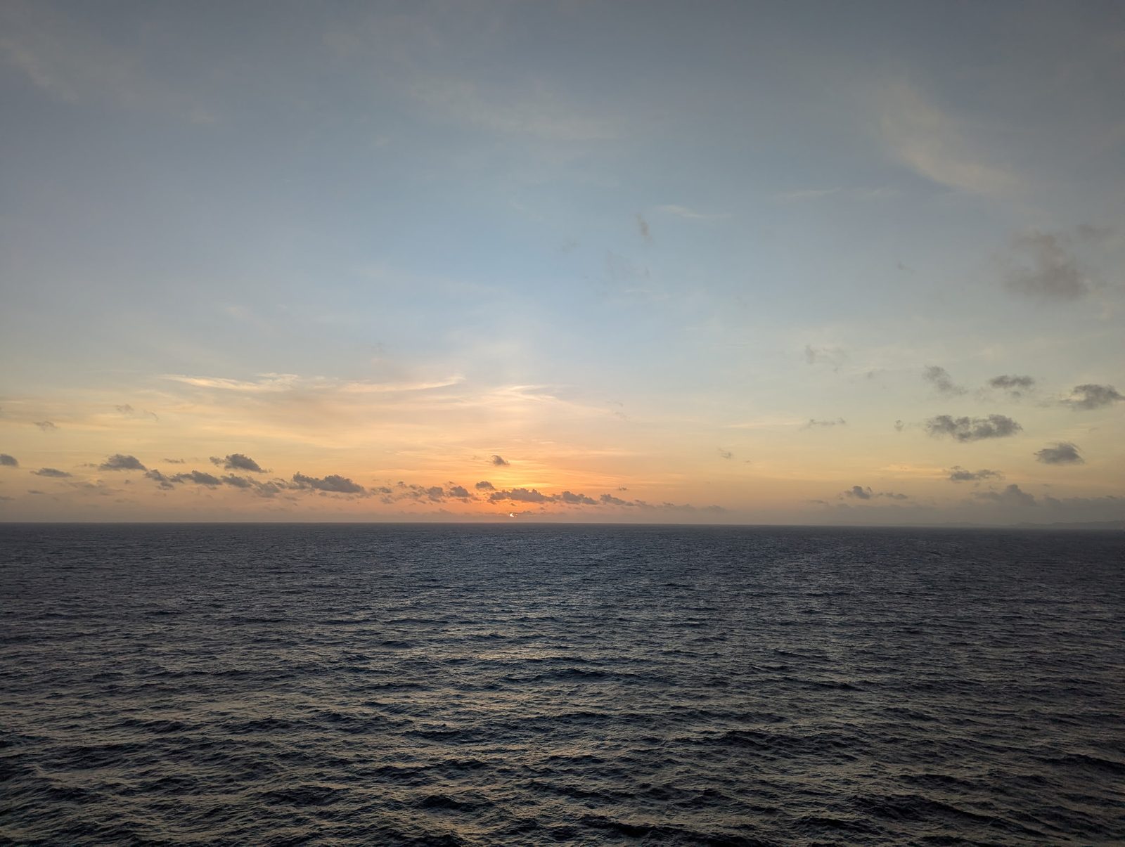 Sunset over open ocean, the sky washed in orange and gold